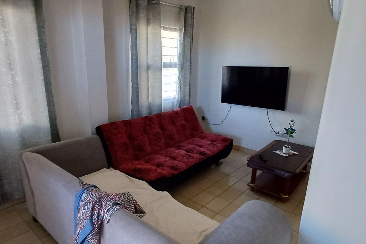 A functional living room featuring tiled flooring and a wall-mounted television, offering a comfortable space for relaxation.