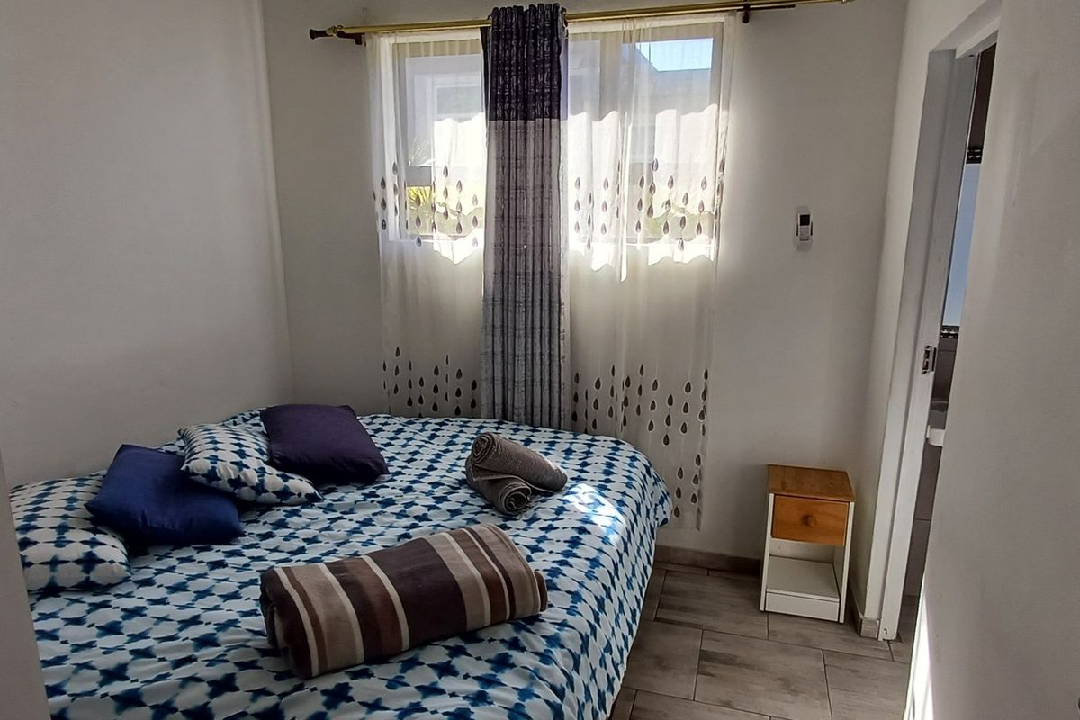 A compact bedroom featuring tiled flooring and a window with a curtain rod, providing a functional sleeping space.