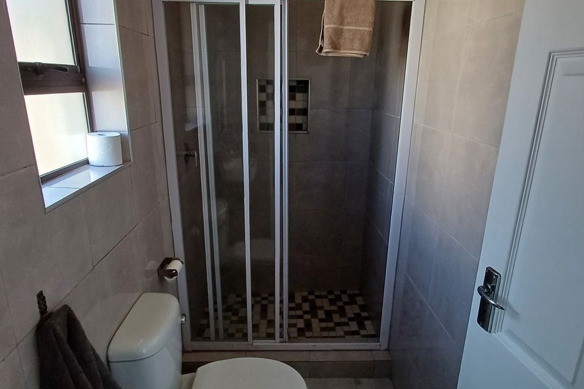A functional bathroom featuring a tiled shower enclosure with a built-in niche, a standard toilet, and neutral wall tiling.