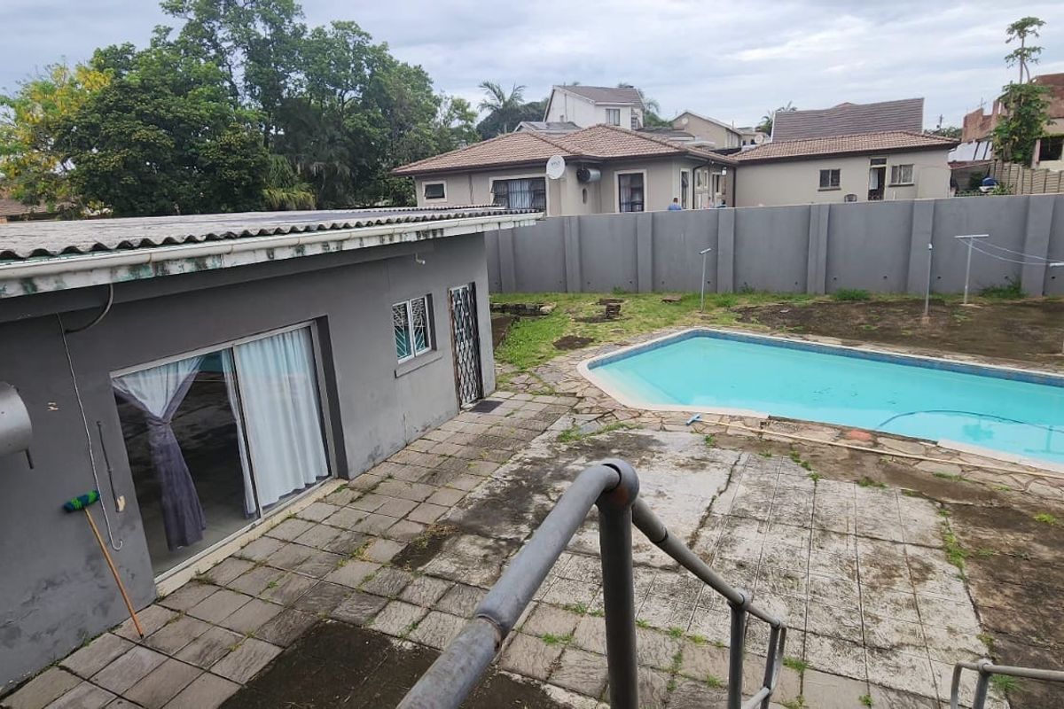 Rear exterior view featuring a swimming pool, paved patio area, and a detached structure with sliding glass doors and an external geyser.