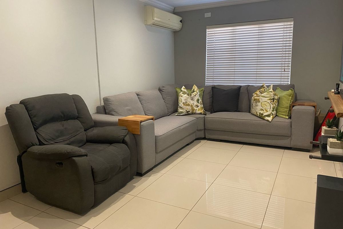 A comfortable living room featuring large format floor tiles, a wall-mounted air conditioning unit, and venetian blinds.