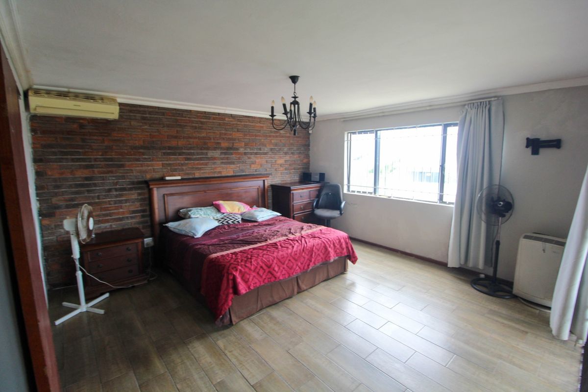 Spacious bedroom featuring a rustic exposed brick feature wall, tiled flooring, and a large window with security bars.