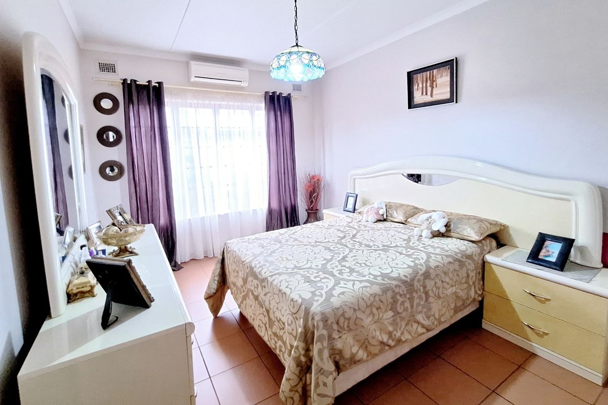 A well-maintained bedroom featuring tiled flooring, a split-system air conditioning unit, and a central pendant light fixture.