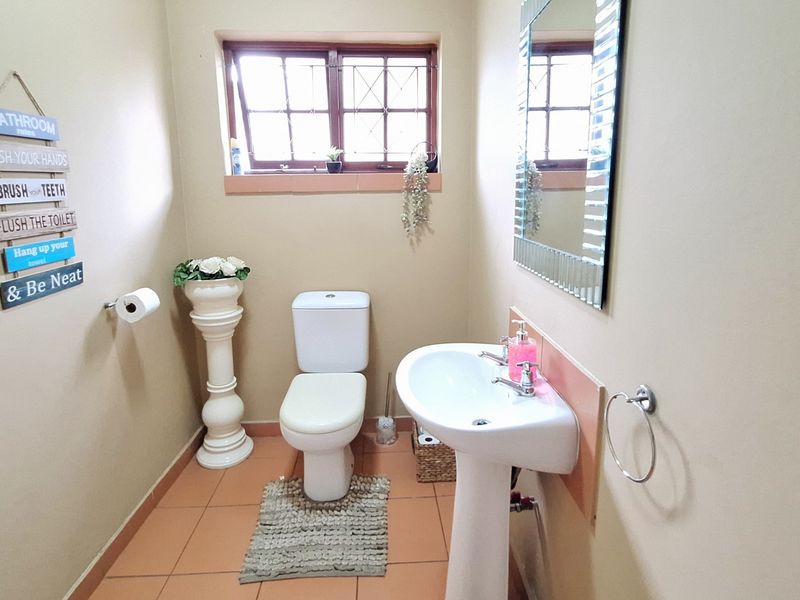 A functional bathroom featuring a pedestal basin, toilet, and tiled flooring with a window providing natural light.
