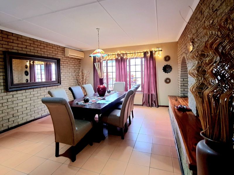 Spacious dining room featuring exposed brick walls, tiled flooring, and a built-in wooden shelf, offering a warm and rustic atmosphere.