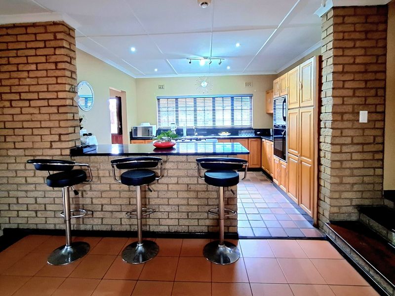 Spacious kitchen featuring a brick breakfast bar, built-in cabinetry, integrated oven, and tiled flooring, framed by distinctive exposed brick pillars.