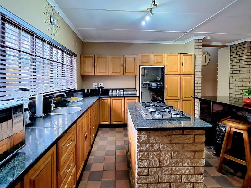 A functional kitchen featuring wooden cabinetry, granite countertops, a central brick island with a built-in gas hob, and tiled flooring.