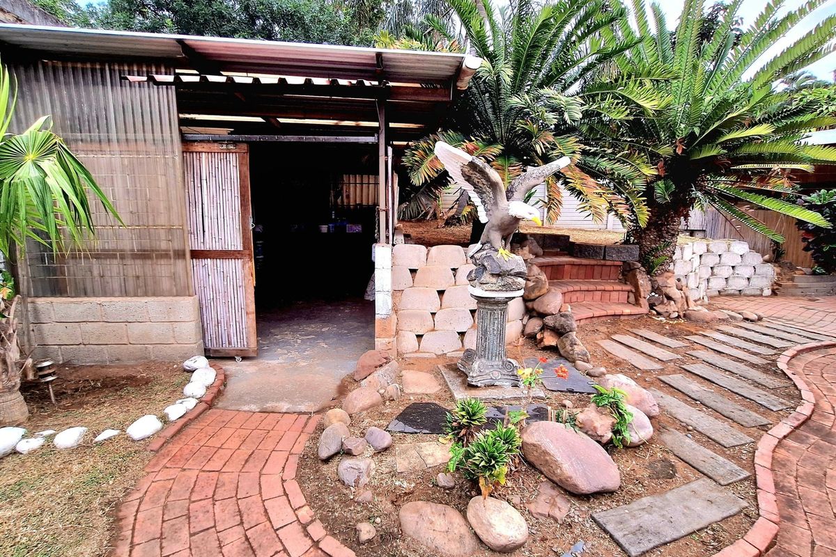Rear garden area featuring a covered outdoor structure, brick paved pathways, and landscaped stone features with a retaining wall.