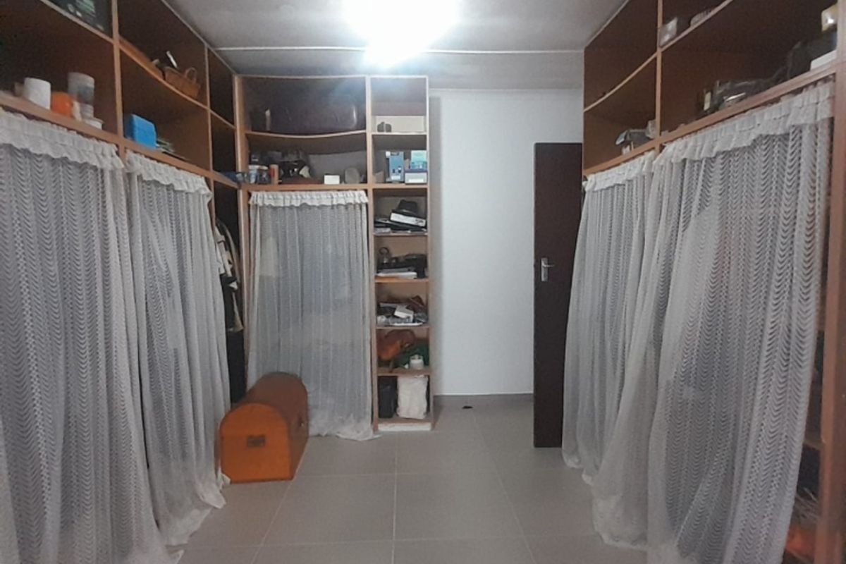 A walk-in closet or bedroom area featuring extensive built-in wooden shelving and storage units with curtained enclosures and neutral tiled flooring.