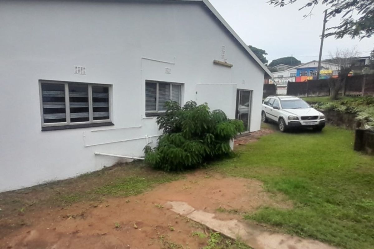 Rear view of the property showing the exterior wall, aluminium windows, and a grassed garden area with a concrete pathway.