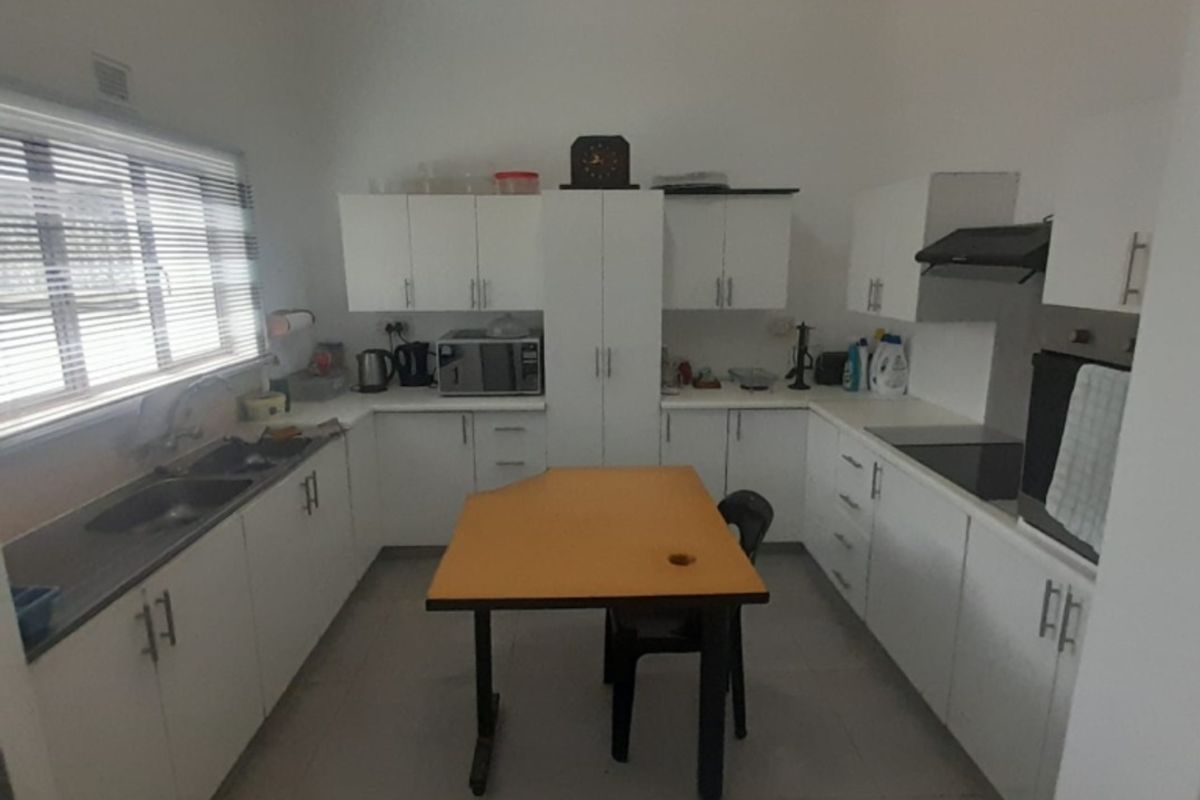 A functional kitchen featuring white built-in cabinetry, integrated oven, extractor fan, and tiled flooring with ample counter space.