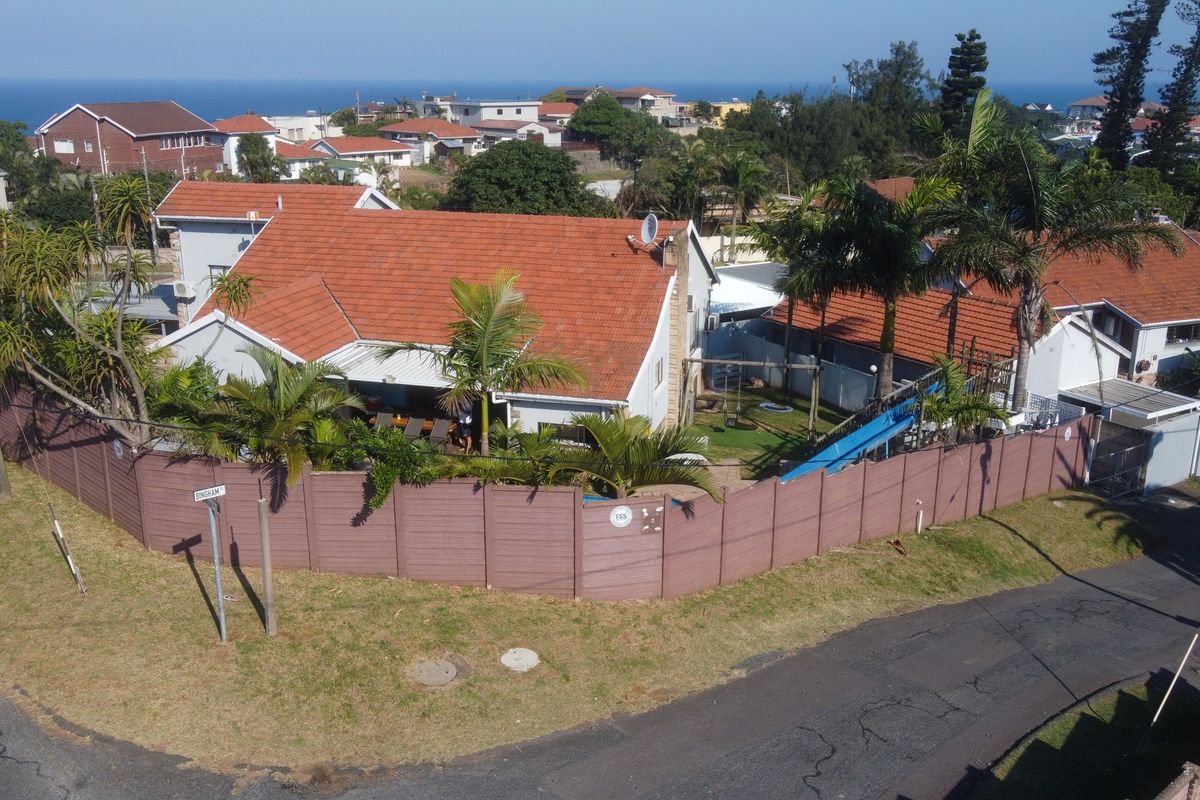 Aerial view of a residential property featuring a tiled roof house, swimming pool, and secure perimeter walling in a coastal neighborhood.