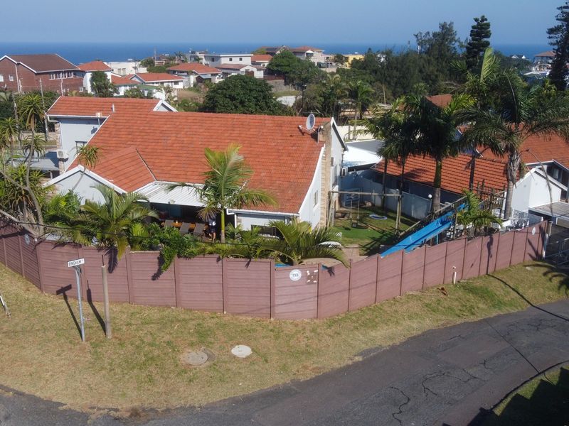Aerial view of a residential property featuring a tiled roof house, swimming pool, and secure perimeter walling in a coastal neighborhood.