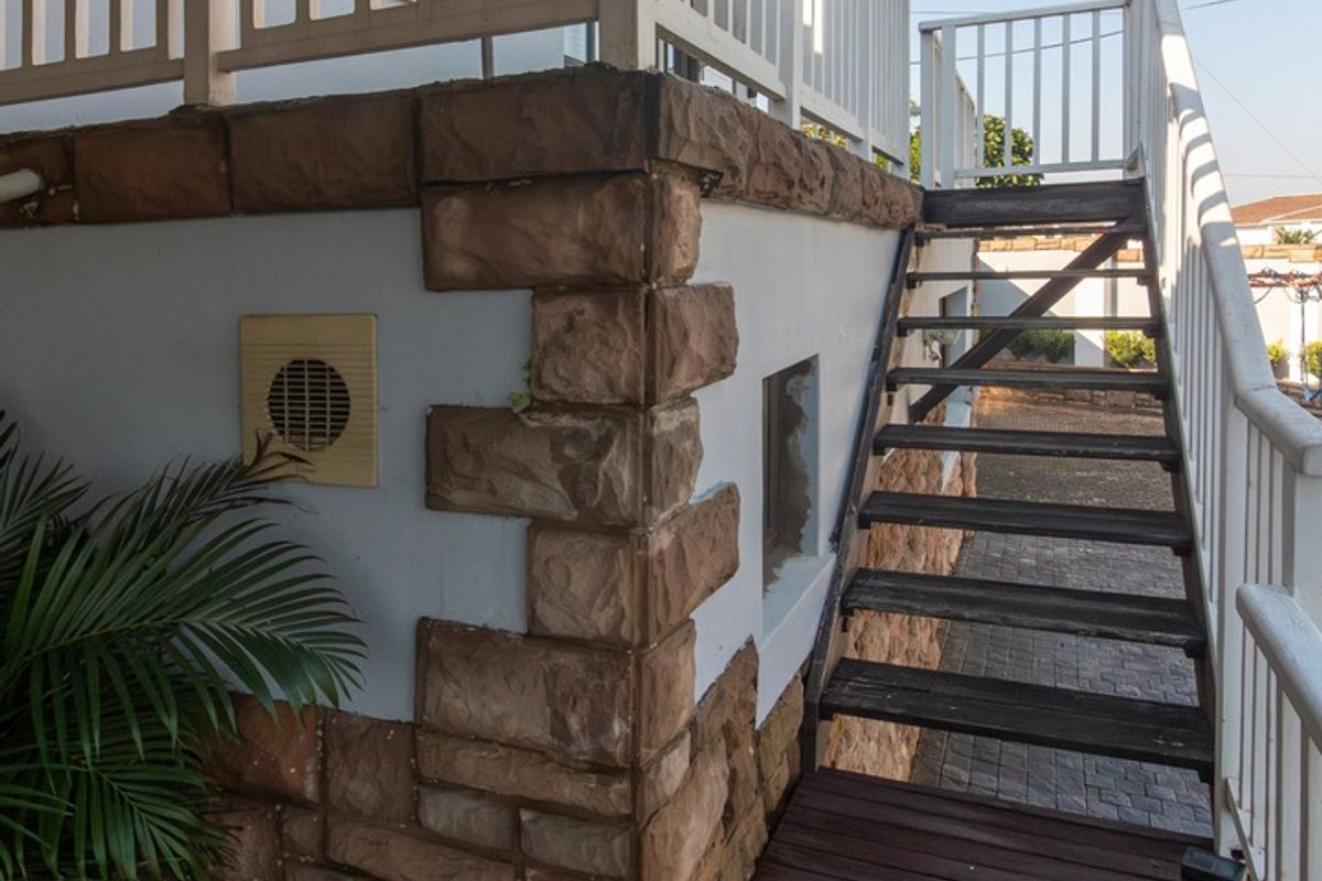 Exterior view of a raised deck featuring stone cladding, a timber staircase, and white balustrades leading to an elevated outdoor area.
