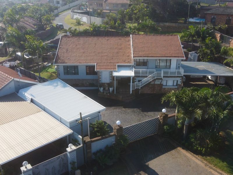 Aerial view of a residential property featuring a tiled roof, paved driveway, secure perimeter wall, and an attached carport.
