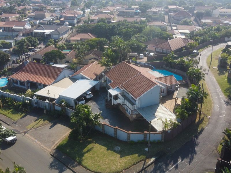 Aerial view of a residential property featuring a tiled roof, swimming pool, carport, and paved driveway within a suburban neighborhood setting.
