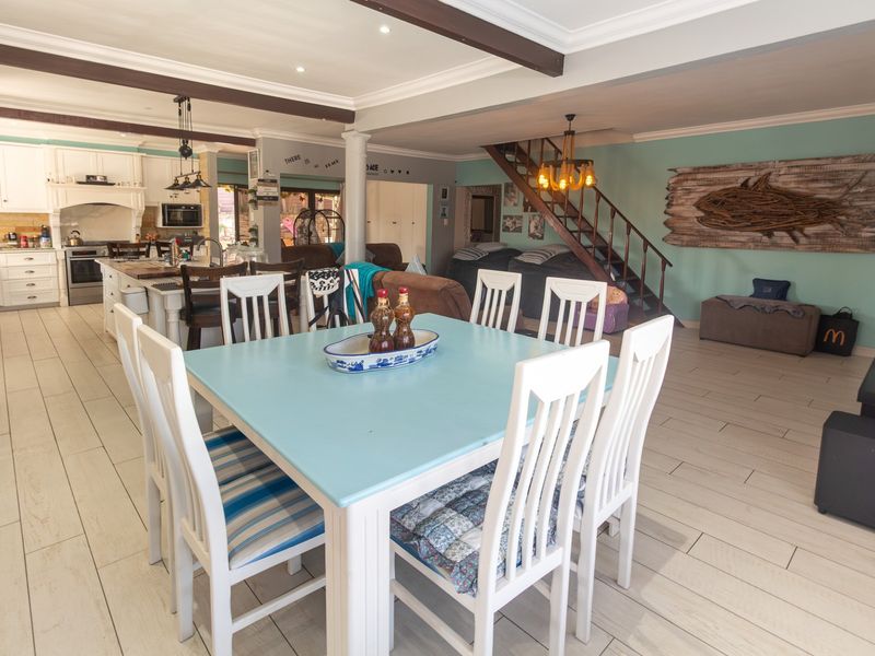 Spacious open-plan living and dining area featuring a functional kitchen with island, exposed ceiling beams, and a wooden staircase leading to the upper level.