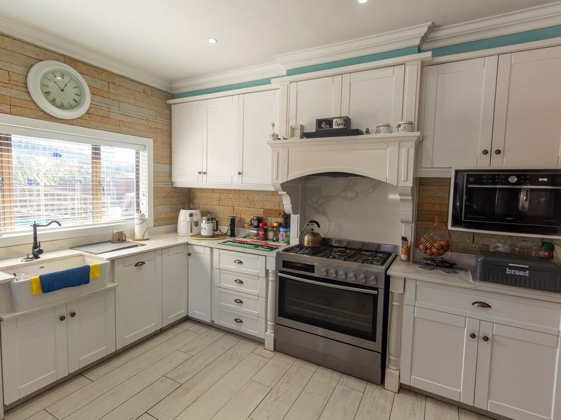 A well-appointed kitchen featuring white cabinetry, a farmhouse sink, gas stove with extractor hood, built-in microwave, and decorative stone veneer wall accents.
