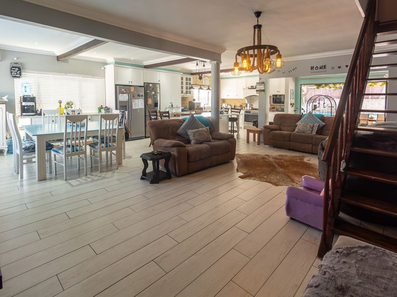 Spacious open-plan living area featuring light-toned tiled flooring, a modern kitchen with island, and a wooden staircase leading to the upper level.