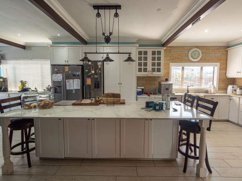 Spacious kitchen featuring a large central island with stone countertops, shaker-style cabinetry, exposed ceiling beams, and a decorative stone feature wall.