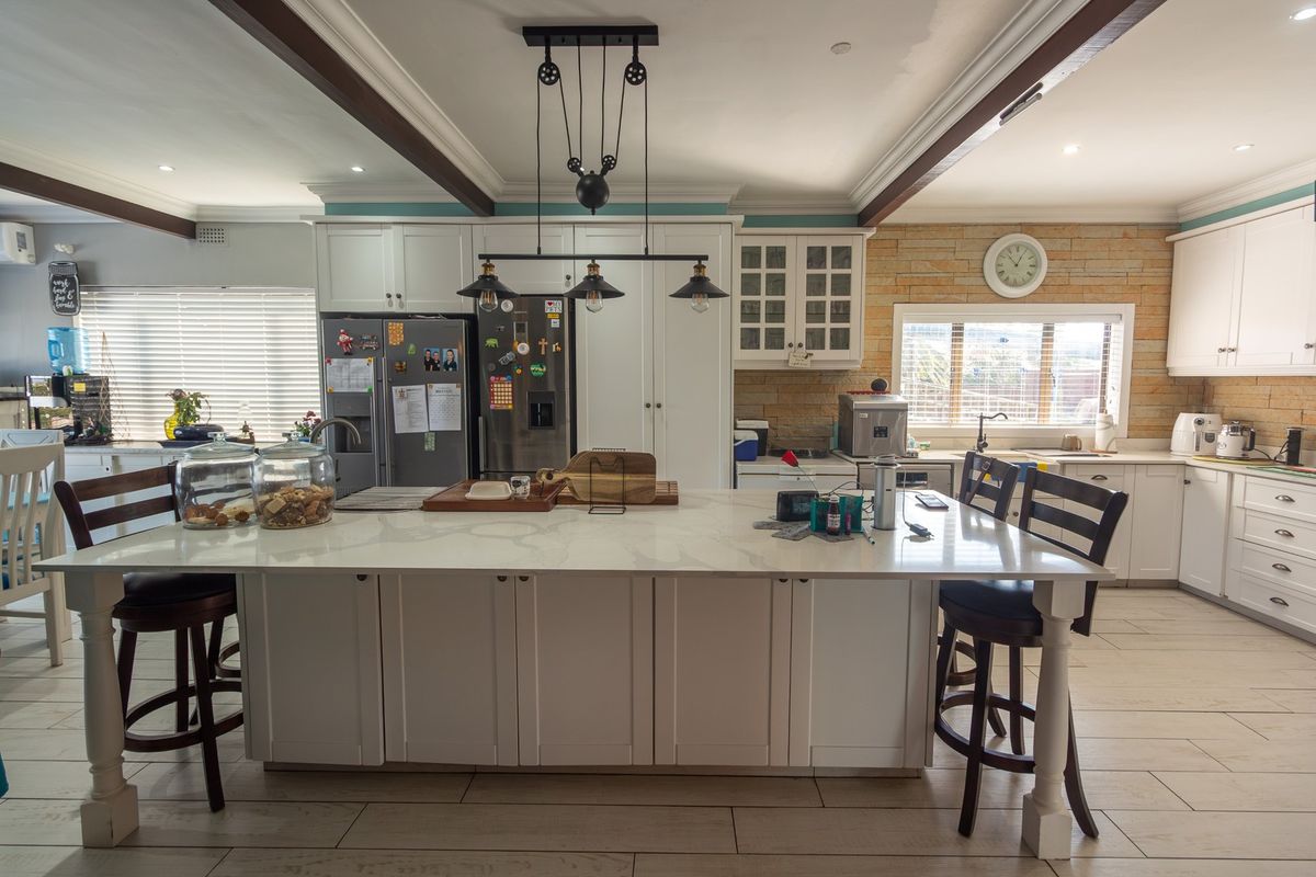 Spacious kitchen featuring a large central island with stone countertops, shaker-style cabinetry, exposed ceiling beams, and a decorative stone feature wall.