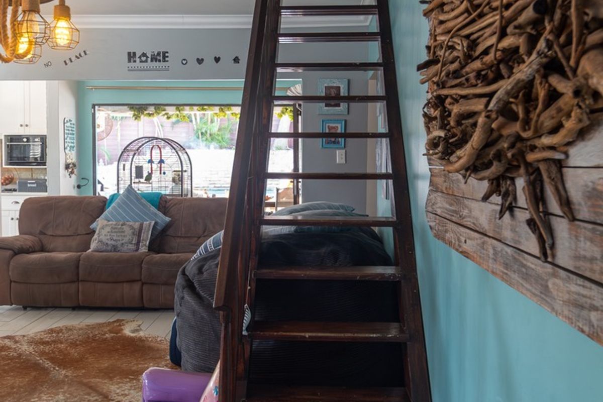 A living area featuring a prominent wooden staircase, light-colored tiled flooring, and crown molding, with an open view toward the rear of the property.