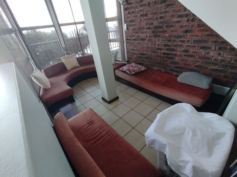 A living area featuring exposed brickwork, large windows providing natural light, and ceramic tiled flooring, offering a unique architectural character.