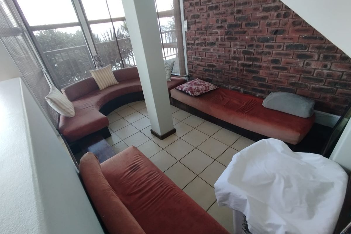 A living area featuring exposed brickwork, large windows providing natural light, and ceramic tiled flooring, offering a unique architectural character.