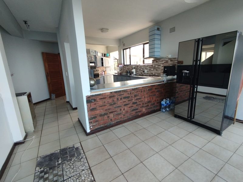 Open plan kitchen area featuring an exposed brick breakfast bar, tiled flooring, and built-in cabinetry with a tiled backsplash.