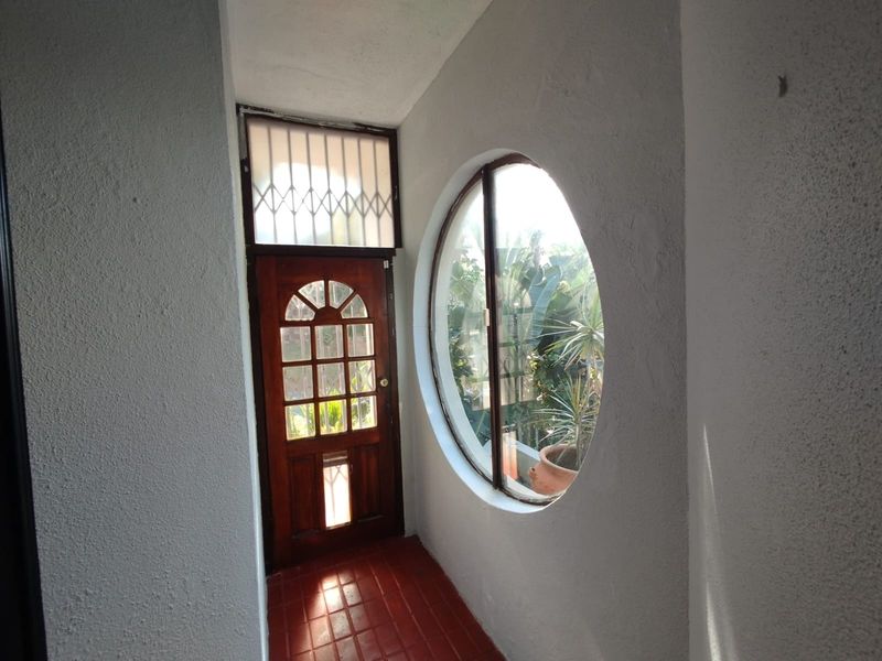 Entrance foyer featuring a distinctive circular window, timber front door with security gate, and terracotta tiled flooring.