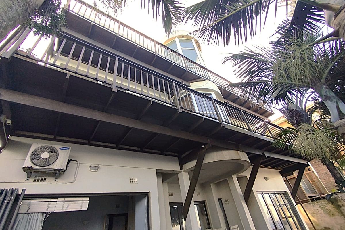 Rear elevation of a multi-story house featuring extensive timber balconies, metal railings, and sliding glass doors leading to the ground floor patio area.