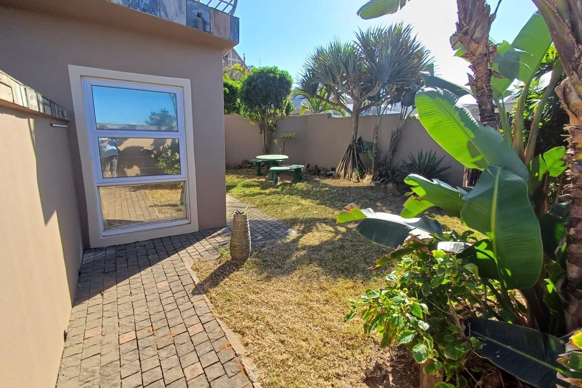 A private rear garden area featuring a paved walkway, established landscaping, and a boundary wall, providing a quiet outdoor space for the townhouse.