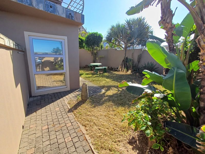 A private rear garden area featuring a paved walkway, established landscaping, and a boundary wall, providing a quiet outdoor space for the townhouse.