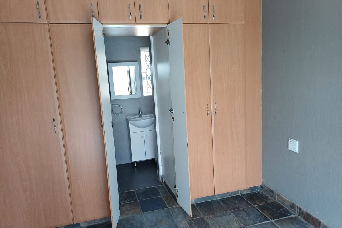 A bedroom featuring built-in wooden cupboards, slate tile flooring, and direct access to an en-suite bathroom with a vanity unit.