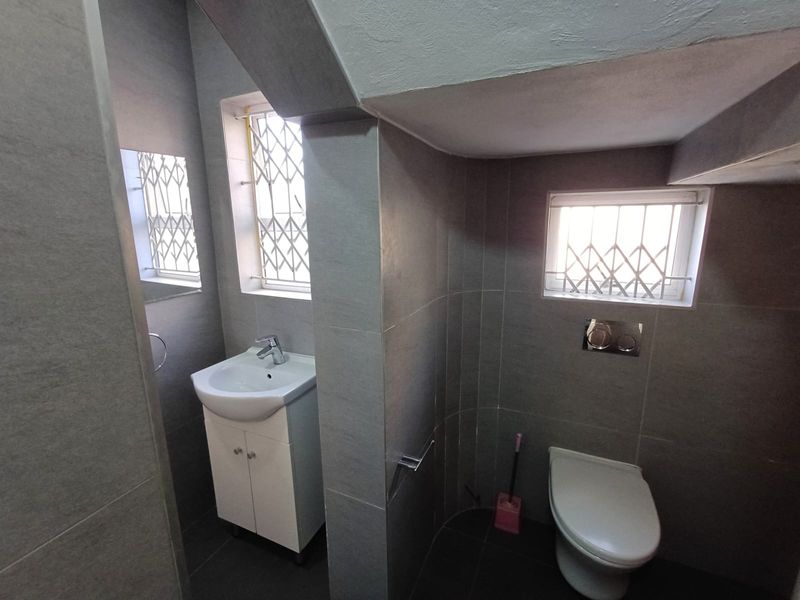 A modern, compact bathroom featuring grey floor-to-ceiling tiling, a wall-mounted toilet, and a vanity basin with a chrome mixer tap.