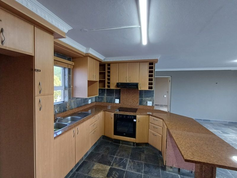 A spacious kitchen featuring light wood cabinetry, granite countertops, a breakfast bar, and slate tile flooring, offering a functional layout ready for modernization.
