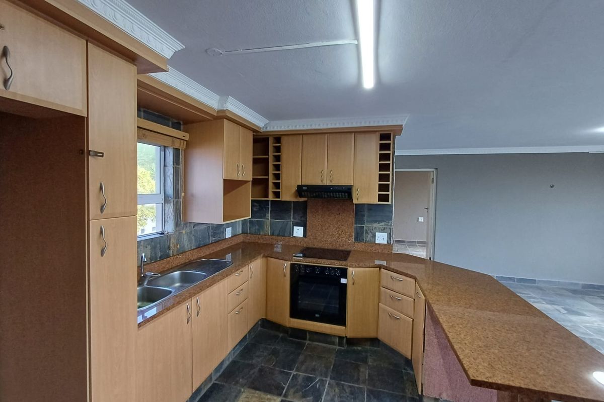 A spacious kitchen featuring light wood cabinetry, granite countertops, a breakfast bar, and slate tile flooring, offering a functional layout ready for modernization.