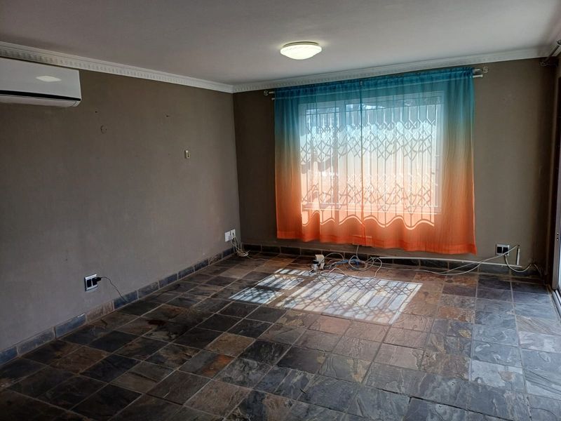 An empty living room featuring slate tile flooring, a wall-mounted air conditioning unit, and a window fitted with a security gate.