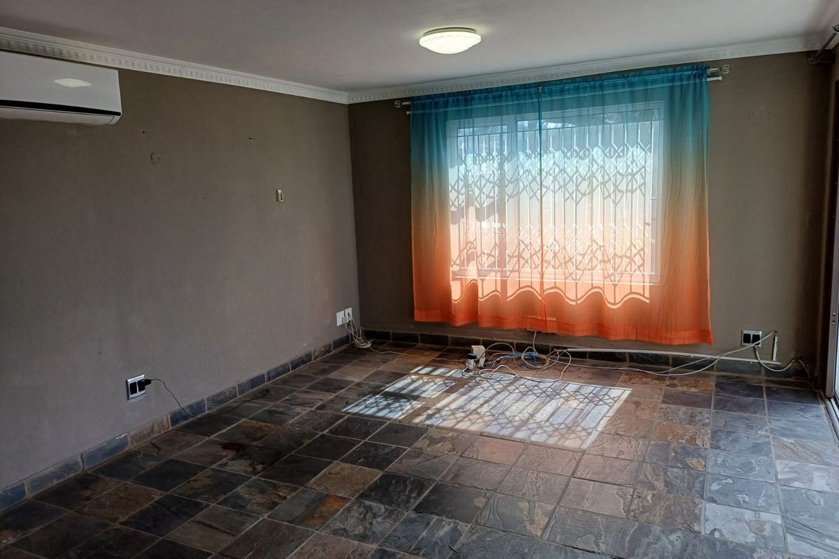 An empty living room featuring slate tile flooring, a wall-mounted air conditioning unit, and a window fitted with a security gate.