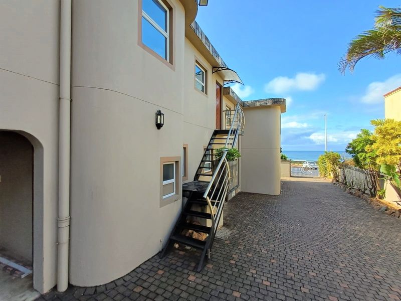 Exterior view of the townhouse featuring a paved driveway, external metal staircase, and ocean views in the background.