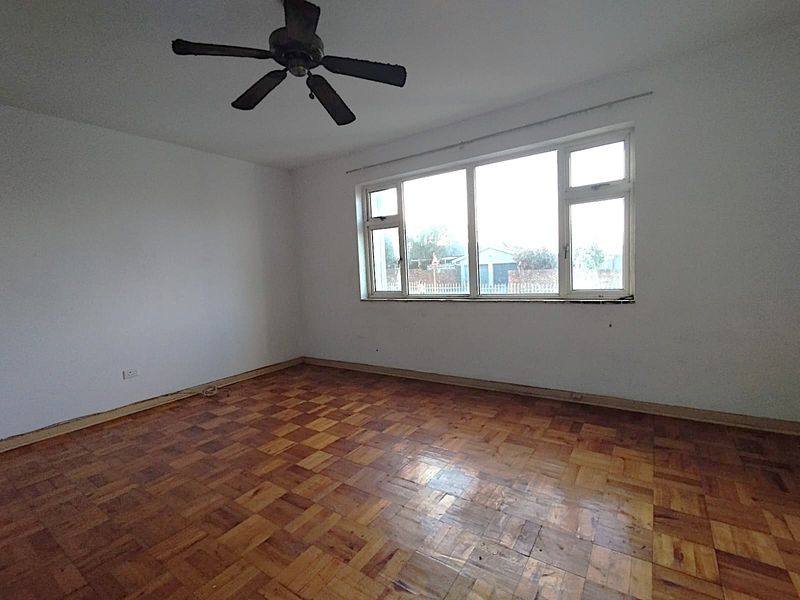 An empty bedroom featuring original parquet flooring, a ceiling fan, and a large window providing natural light.