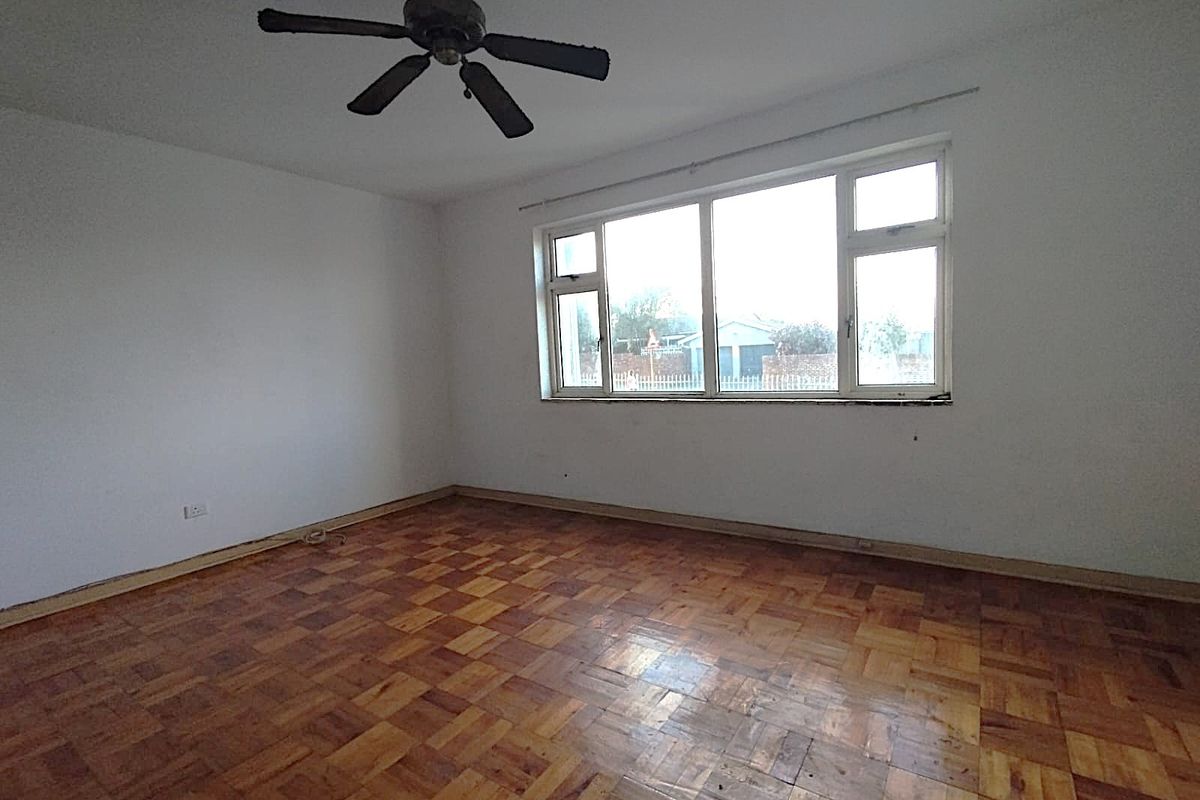 An empty bedroom featuring original parquet flooring, a ceiling fan, and a large window providing natural light.