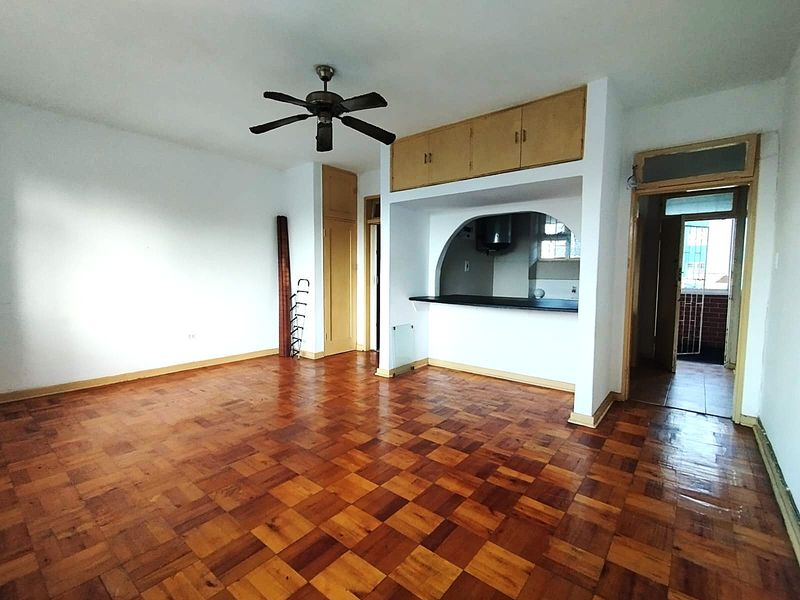 Spacious open-plan living area featuring classic parquet flooring, a ceiling fan, and a functional breakfast bar with overhead built-in cabinetry.