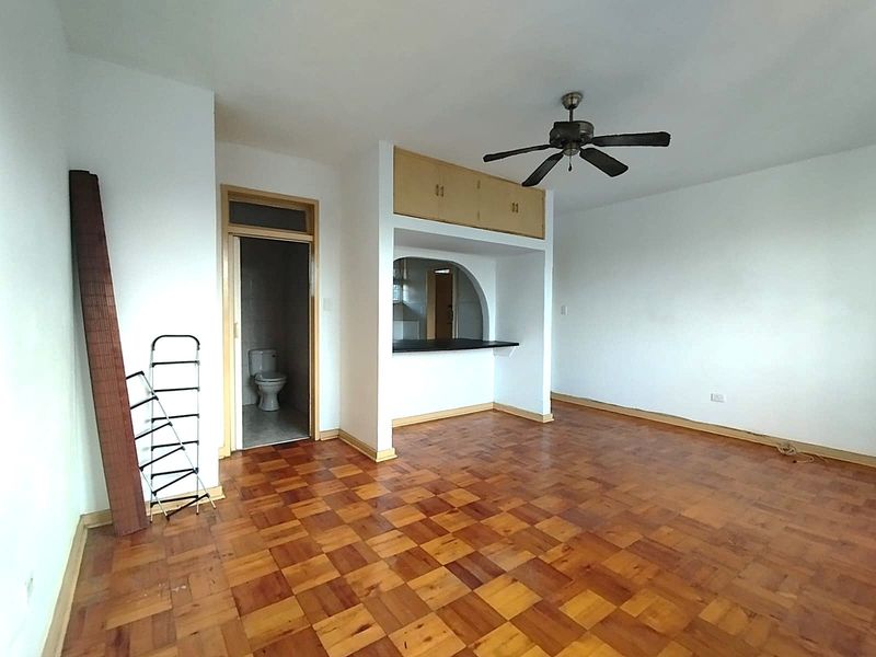 An empty living area featuring parquet flooring, a ceiling fan, and a convenient pass-through window connecting to the kitchen area.