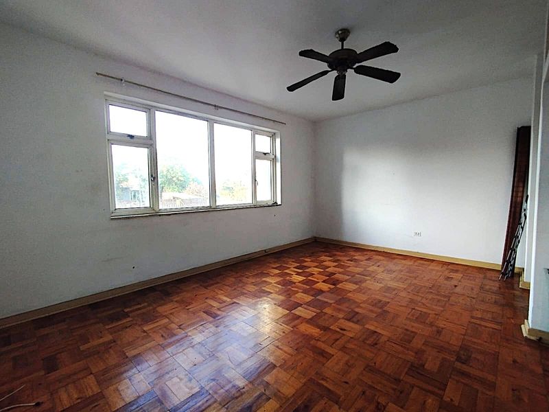 An empty living room featuring original parquet flooring, a ceiling fan, and a large window providing natural light.