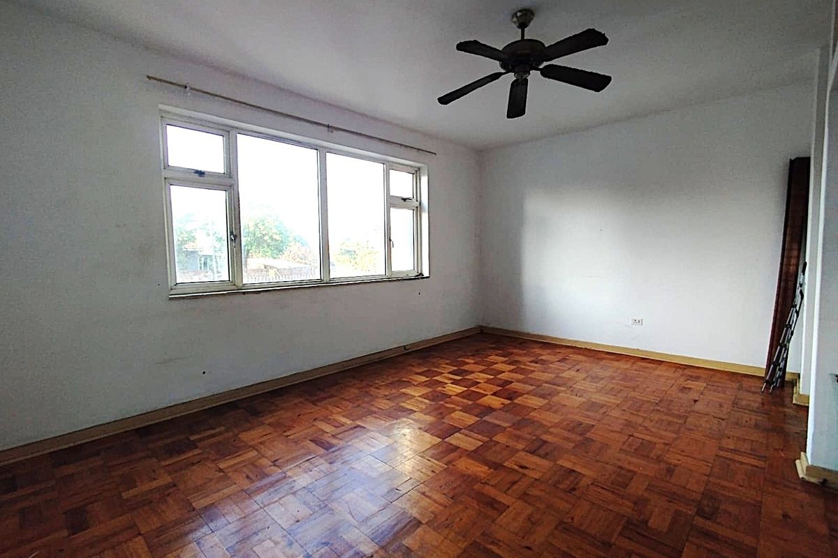 An empty living room featuring original parquet flooring, a ceiling fan, and a large window providing natural light.