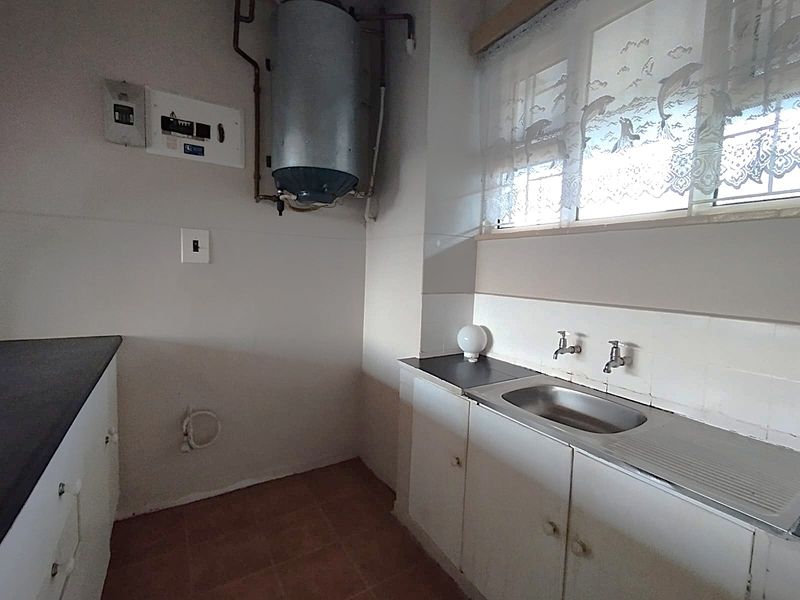 A functional laundry area featuring a stainless steel sink, built-in cabinetry, and an electric water heater, providing essential utility space for the apartment.
