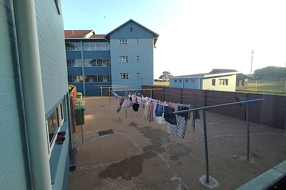 A communal paved rear courtyard area featuring metal washing lines and perimeter walling, serving the apartment complex.