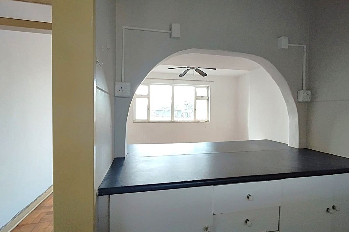 A dated kitchen area featuring a distinctive arched serving hatch, built-in cabinetry, and exposed electrical conduit, opening into an adjacent living space.