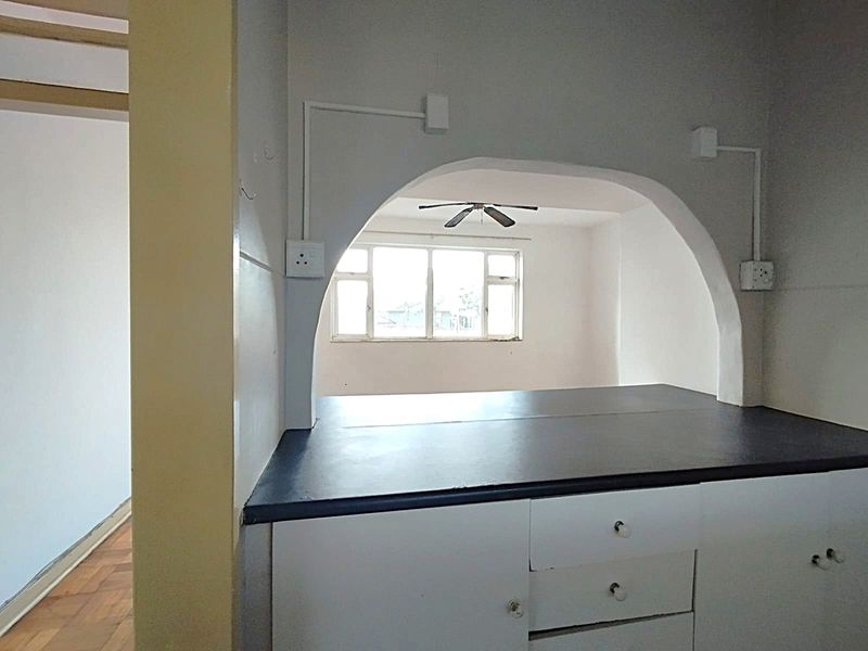 A dated kitchen area featuring a distinctive arched serving hatch, built-in cabinetry, and exposed electrical conduit, opening into an adjacent living space.